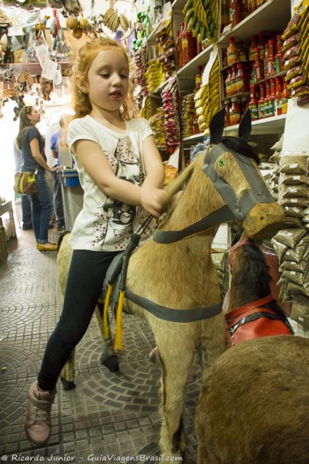Imagem de uma menina em cima de uma cavalo de madeira.